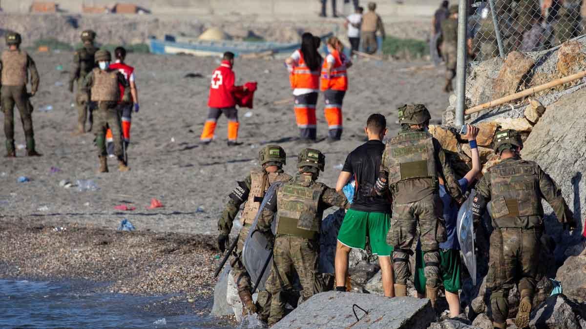 Miembros del ejército ayudan a varios inmigrantes a su llegada a la playa de El Tarajal, junto a la valla fronteriza , en Ceuta este miércoles.