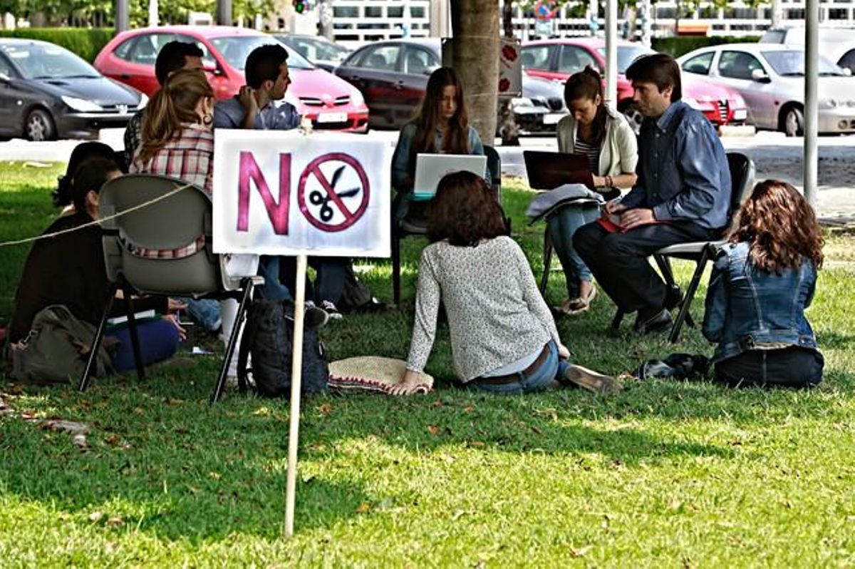 Un grupo de estudiantes da clase al aire libre junto a una camparta contra los recortes en educación Un grupo de estudiantes da clase al aire libre junto a una camparta contra los recortes en educación