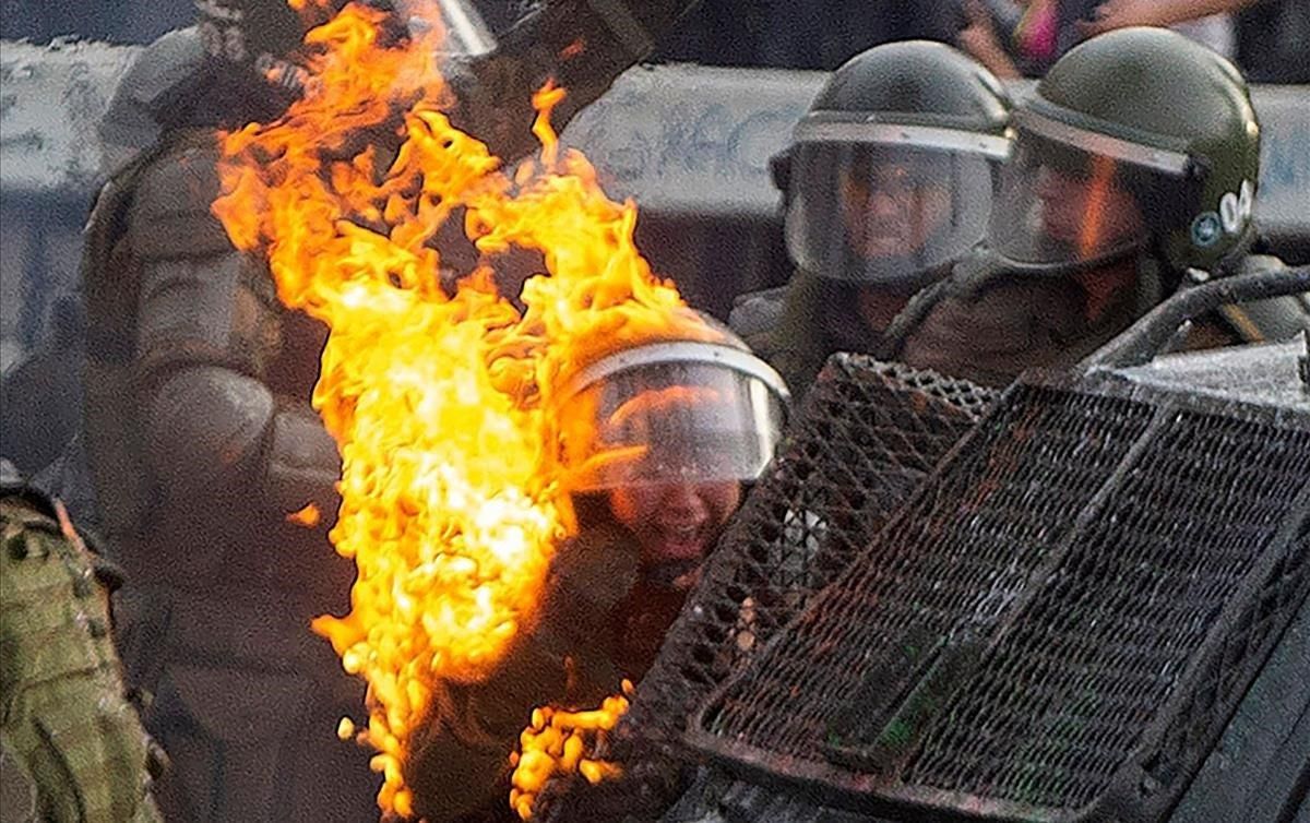 Una bomba de gasolina alcanza a un agente de la policía antidisturbios durante los enfrentamientos con manifestantes que protestan contra las políticas económicas del gobierno, en Santiago Una bomba de gasolina alcanza a un agente de la policía antidisturbios durante los enfrentamientos con manifestantes que protestan contra las políticas económicas del gobierno, en Santiago