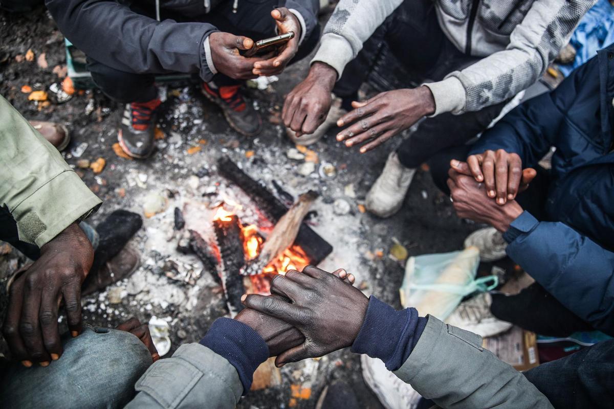 Migrantes calientan sus manos en un campamento en Calais. EFE/EPA/MOHAMMED BADRA