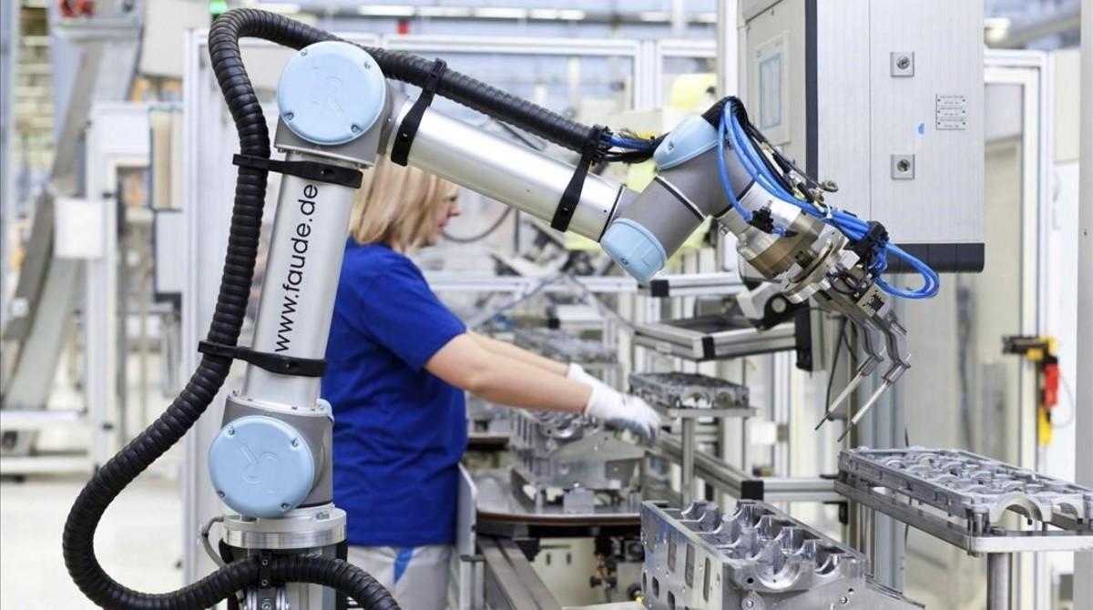 Un brazo robotizado, junto a una trabajadora, en la fábrica de Volkswagen en Salzgitter (Alemania).