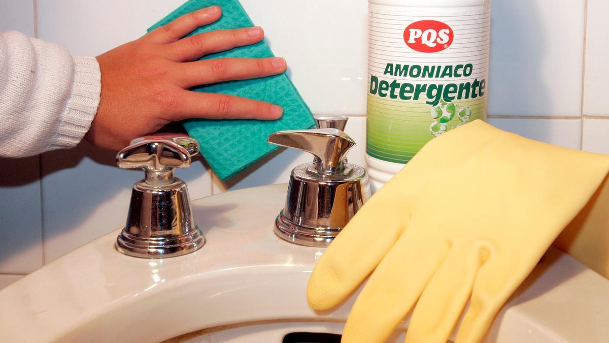 Una persona limpia la grifería de un baño con una bayeta y amoniaco.