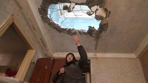 Una mujer de pie en su apartamento muestra el techo dañado por un ataque con misiles rusos en una aldea en la línea del frente de la parte norte de la región de Kiev.