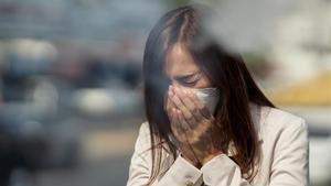 Una mujer tose con una mascarilla puesta.