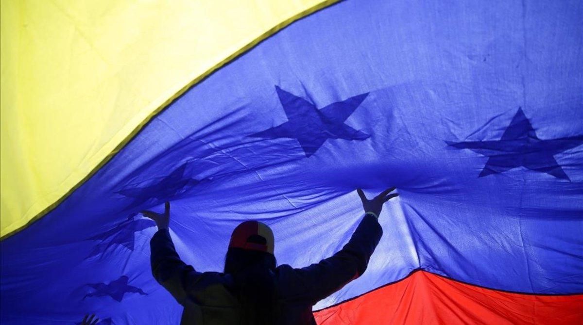 Una mujer sujeta una gran bandera de Venezuela. Una mujer sujeta una gran bandera de Venezuela.