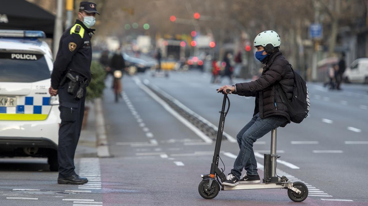Un usuario del patinete eléctrico circula ante un guardia urbano, en Barcelona