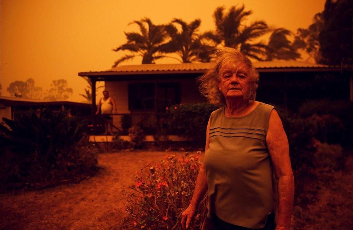 Una mujer mira a la cámara frente a su casa, azotada por los fuertes vientos que empujan el humo de los incendios en Nueva Gales del Sur, Australia Una mujer mira a la cámara frente a su casa, azotada por los fuertes vientos que empujan el humo de los incendios en Nueva Gales del Sur, Australia