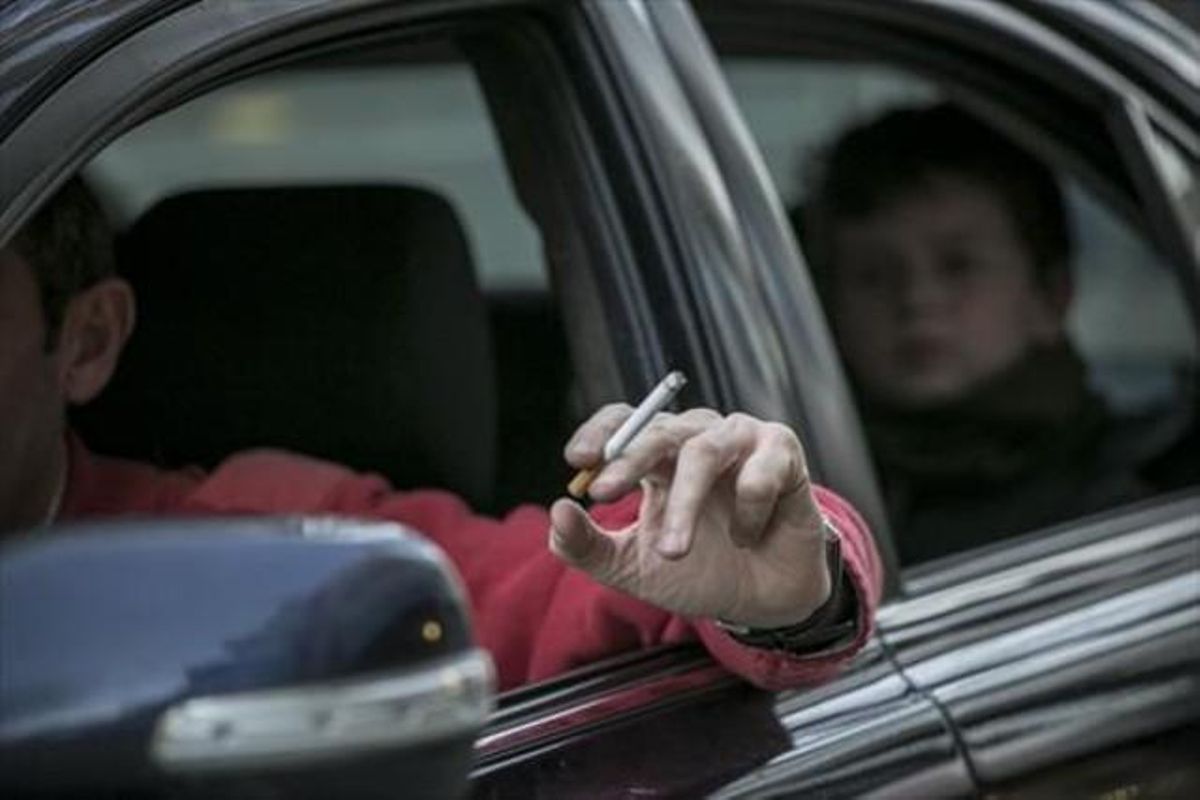 Un conductor fuma un cigarrillo en un coche, con un niño en el asiento de atrás. Un conductor fuma un cigarrillo en un coche, con un niño en el asiento de atrás.
