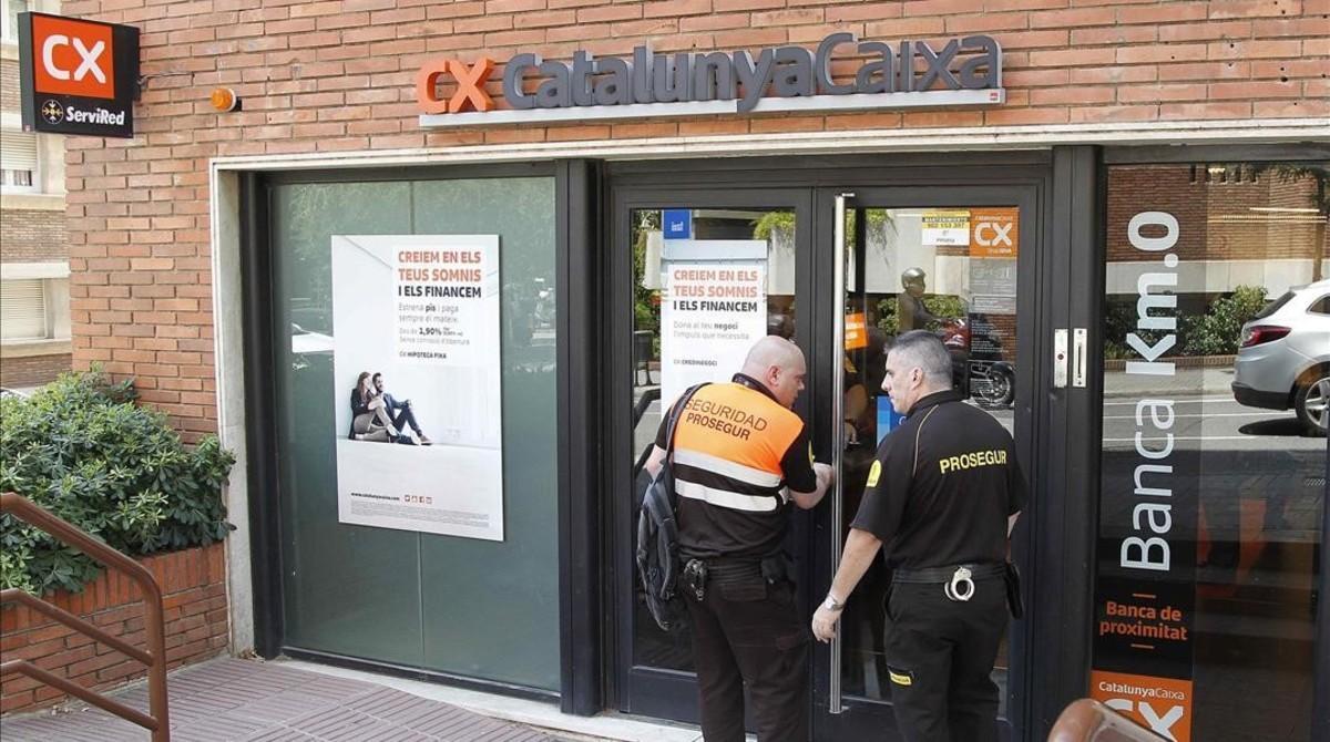 Dos empleados de seguridad entran en el interior de la oficina de CatalunyaCaixa donde se produjo uno de los crímenes. 