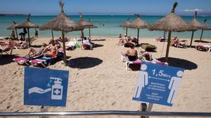 Turistas toman el sol en una playa de Palma de Mallorca, con los carteles en los que se recuerdan las medidas de seguridad en primer plano, este viernes.