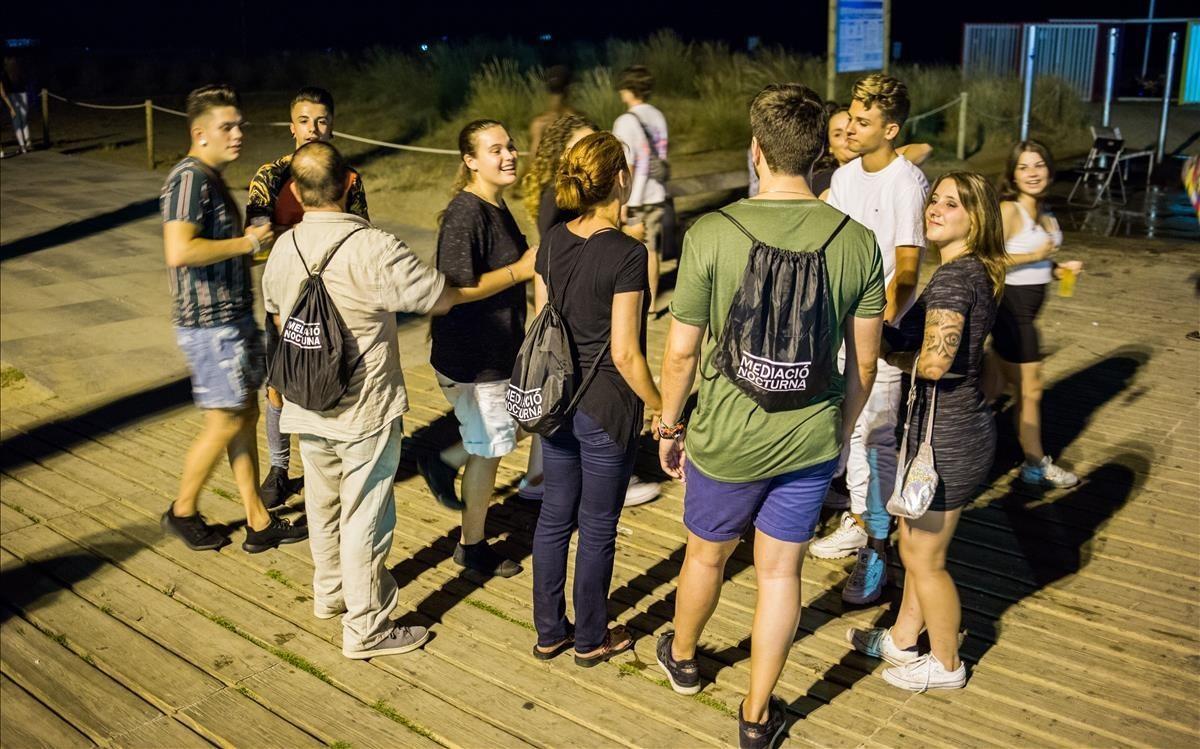 Varios mediadores, con mochilas negras, hablan con jóvenes de botellón en Castelldefels.