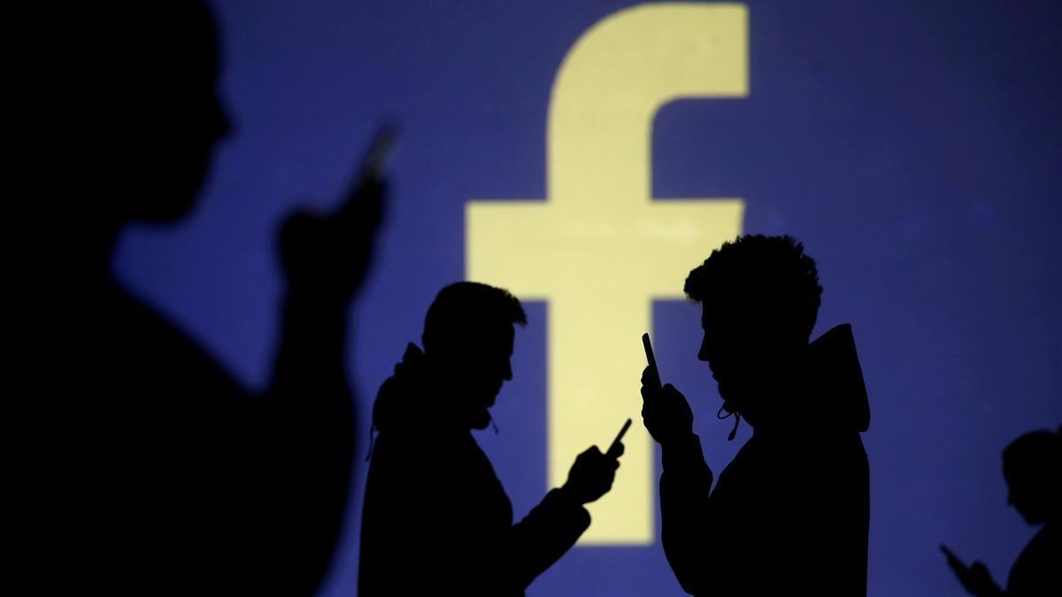 Usuarios de móvil ante el logo de Facebook.