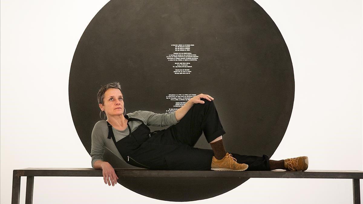 Christina Schultz, artista participante en la exposición  Perder el tiempo y encima procurarse un reloj para este propósito, posa en actitud relajada frente a su obra.