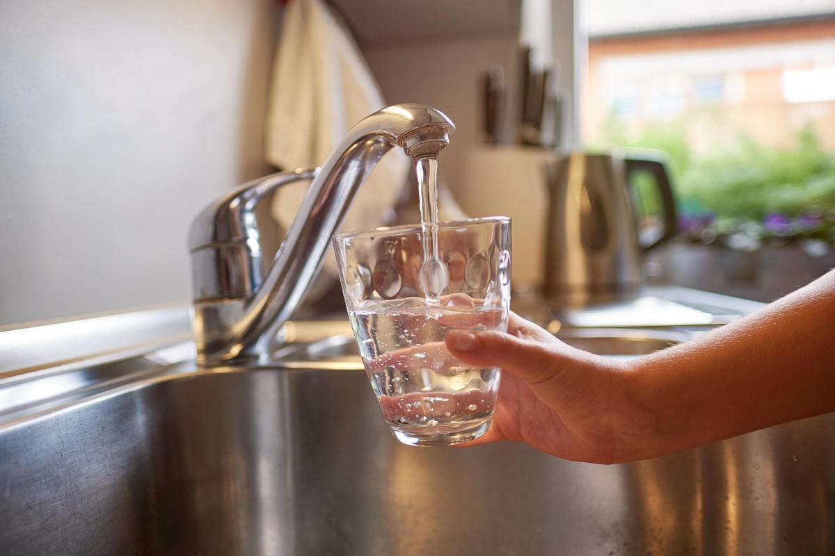 Una persona rellena un vaso con agua de un grifo doméstico. 