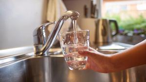 Una persona rellena un vaso con agua de un grifo doméstico. 