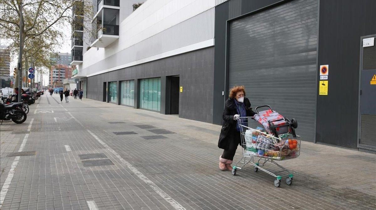 Una mujer enmascarada empuja un carro con la compra por la Gran Via. Una mujer enmascarada empuja un carro con la compra por la Gran Via.