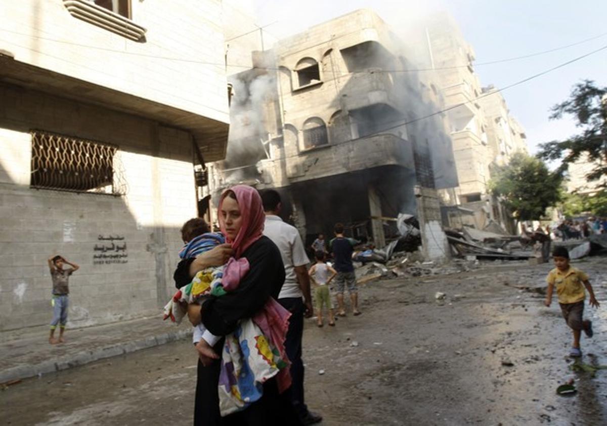 Una mujer palestina corre con su hijo para resguardarse de los ataques israelís, este jueves en Gaza.