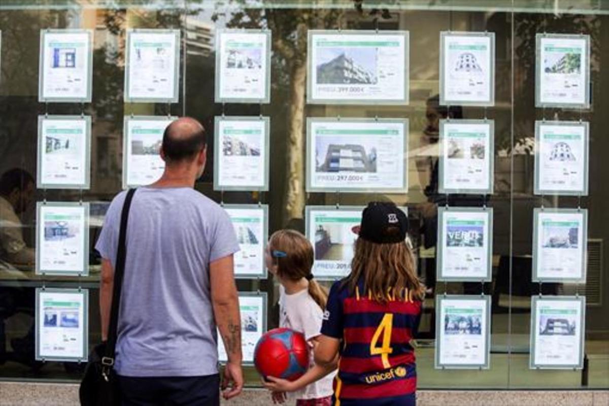 Un hombre y dos niñas observan las ofertas de viviendas en una agencia inmobiliaria del paseo de Maragall de Barcelona.