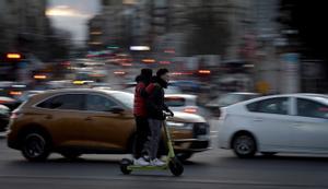 Dos jóvenes desafían al tráfico con un patín eléctrico en el centro de Madrid.
