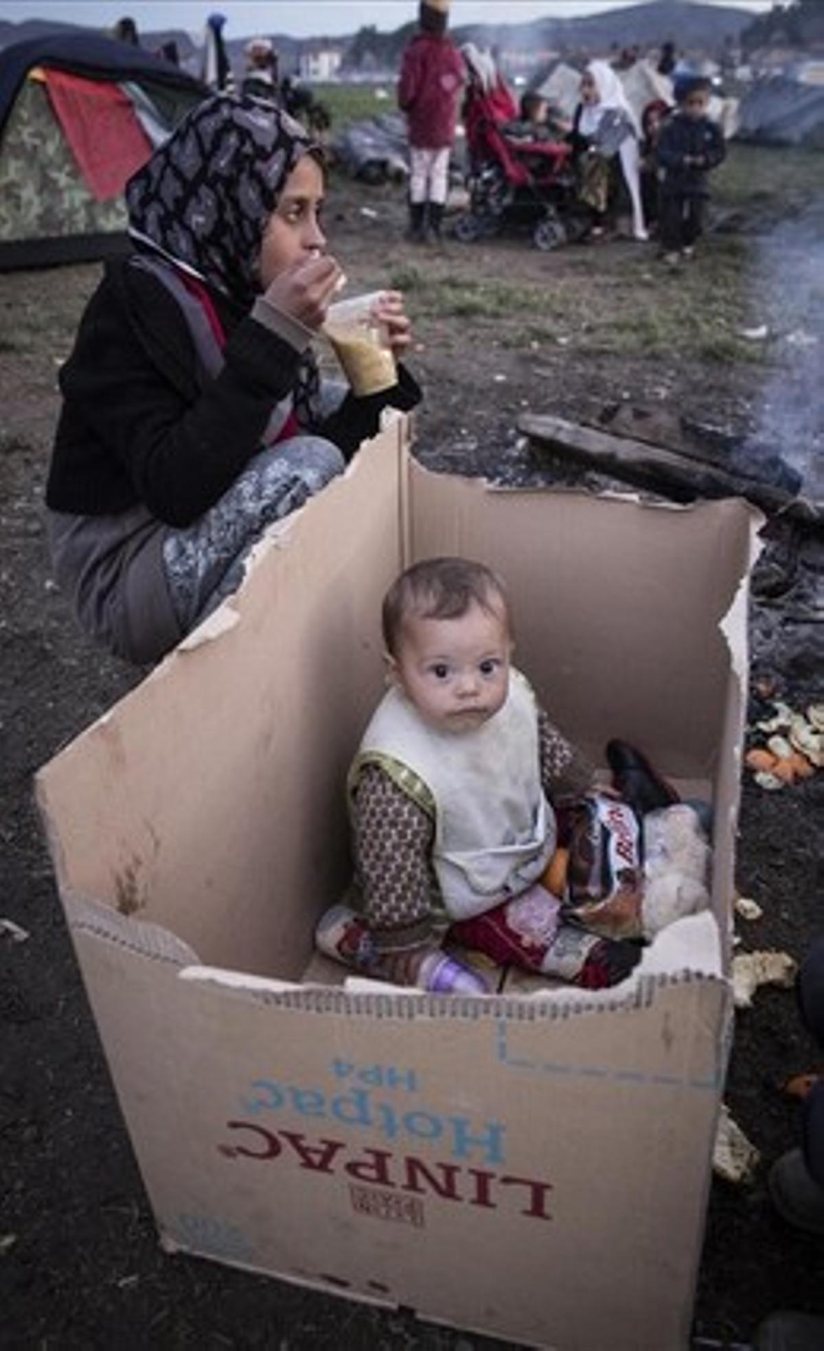 Un bebé sirio en un parquecito improvisado con una caja de cartón en medio del barrizal de Idomeni.