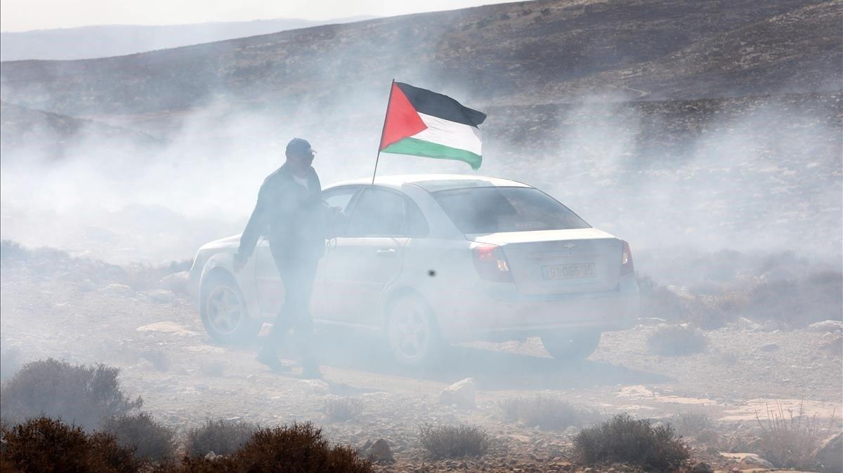 Un hombre ondea la bandera palestina entre gas lacrimógeno, este domingo durante una protesta en el pueblo cisjordano de Shiyoukh, cercano a Hebrón.