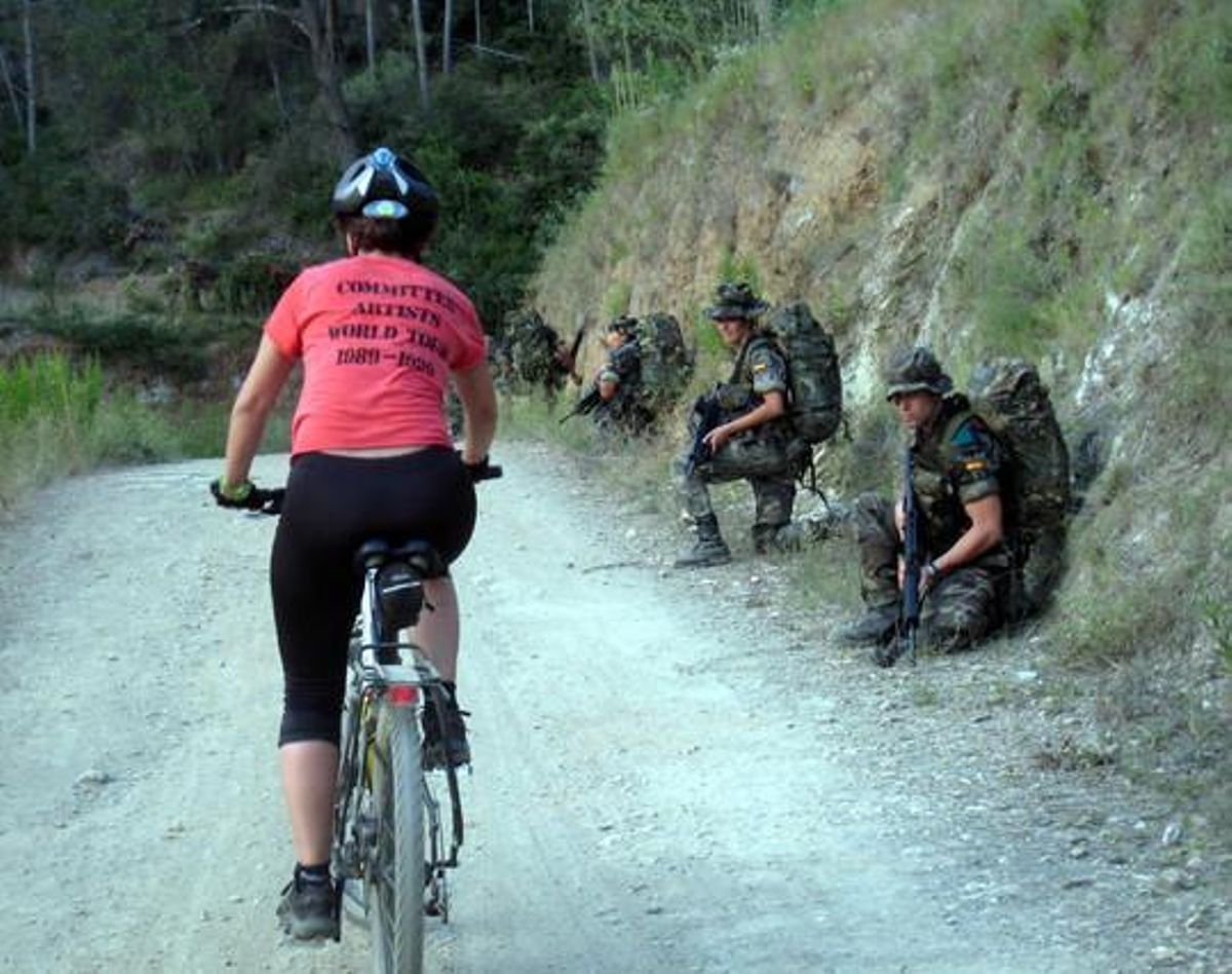 Una ciclista pasa ante soldados en pleno ejercicio de prácticas de combate. Una ciclista pasa ante soldados en pleno ejercicio de prácticas de combate.