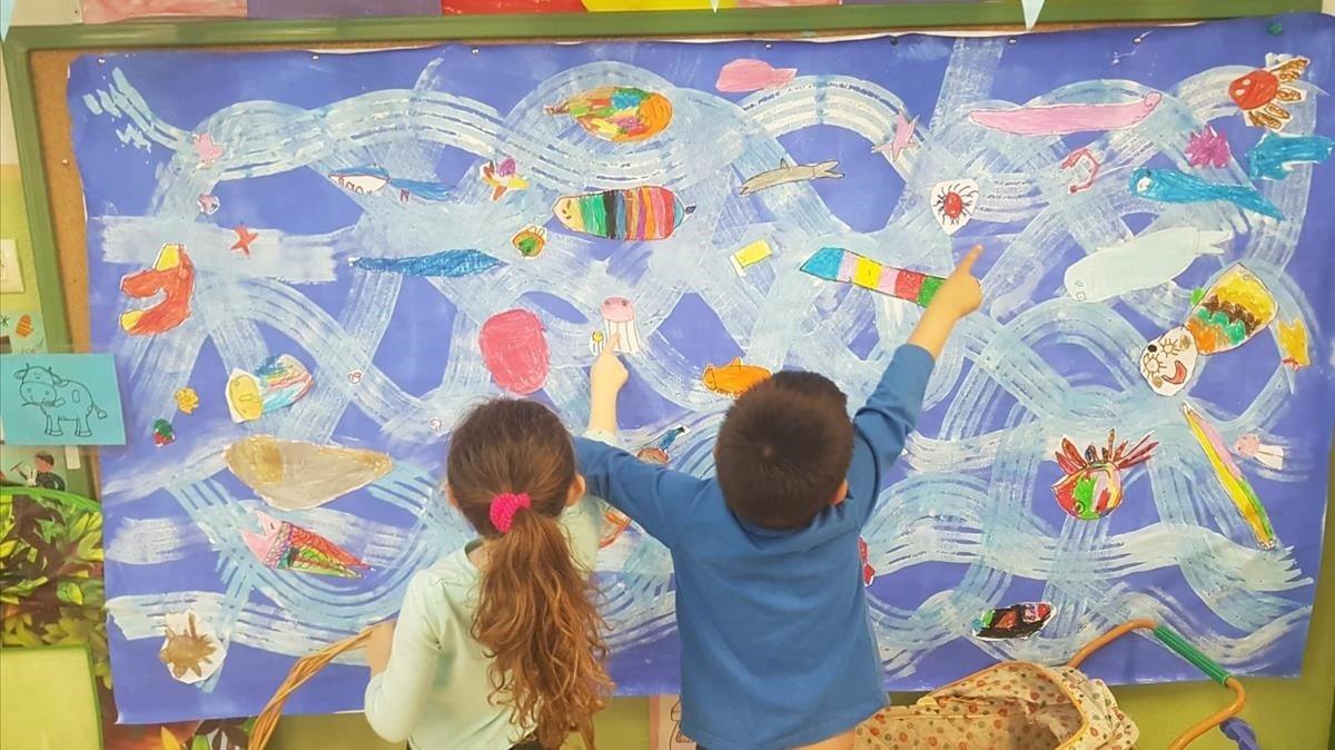 Dos niños observan un mural que pintaron en clase para retratar la variedad de especies que existen en el fondo del mar.
