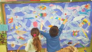 Dos niños observan un mural que pintaron en clase para retratar la variedad de especies que existen en el fondo del mar.