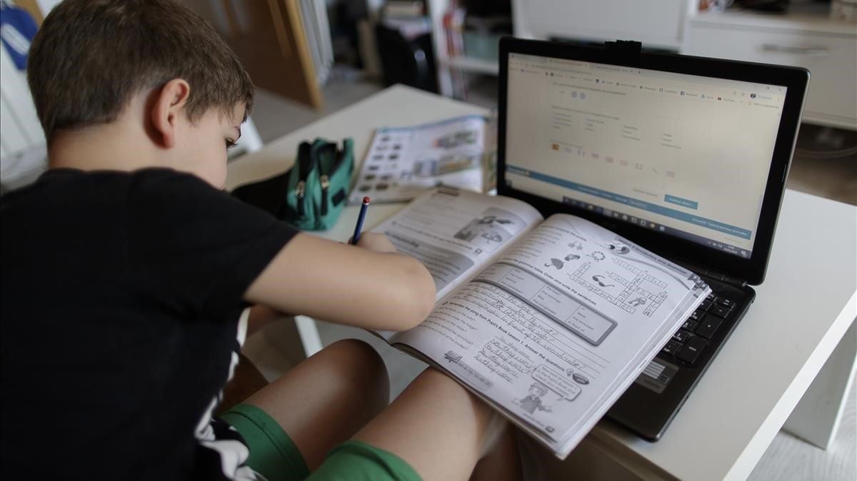 Un niño realiza sus deberes con un portátil en su casa, durante el confinamento. Un niño realiza sus deberes con un portátil en su casa, durante el confinamento.
