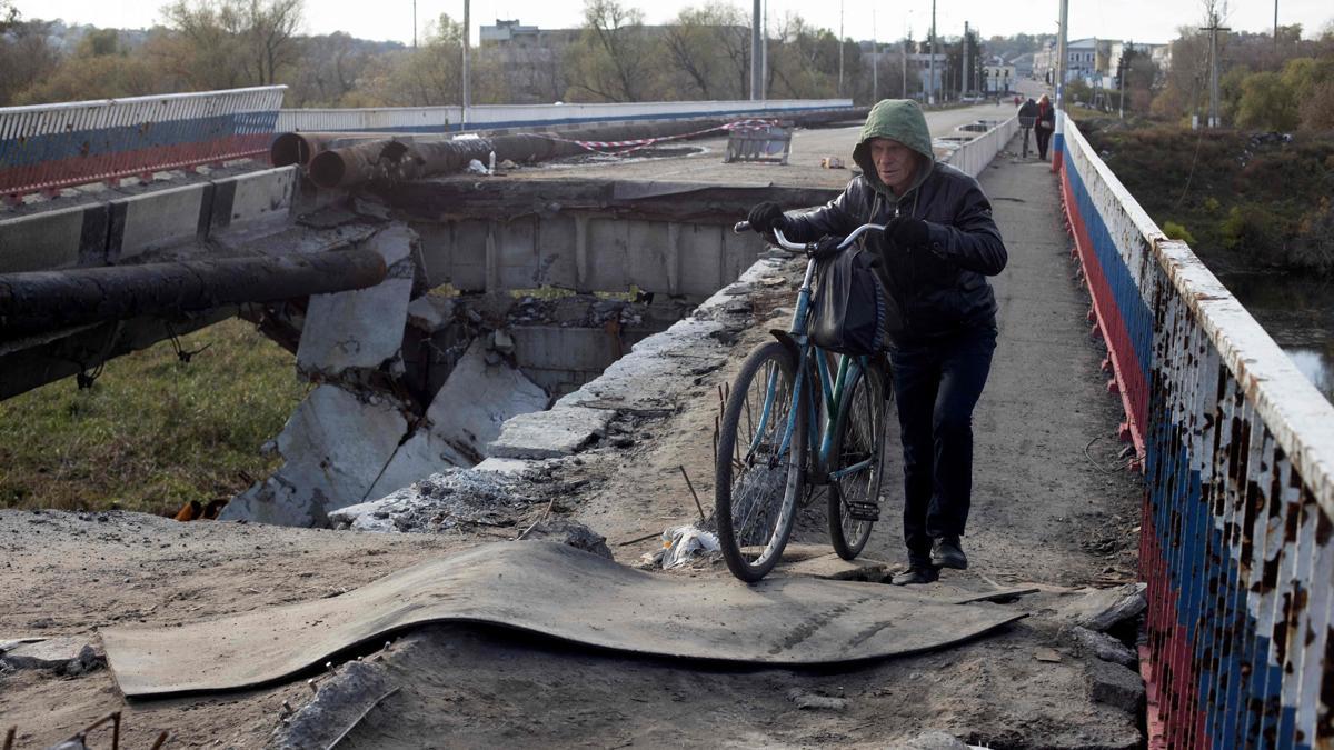 Un residente de Borivske, en la región de Járkov, pasa con su bicicleta sobre un puente destruido por los bombardeos.