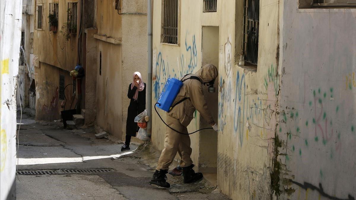 Una mujer palestina cubre su cara con un pañuelo mientras un trabajador de protección civil desinfecta un portal, el pasado día 16 de marzo.