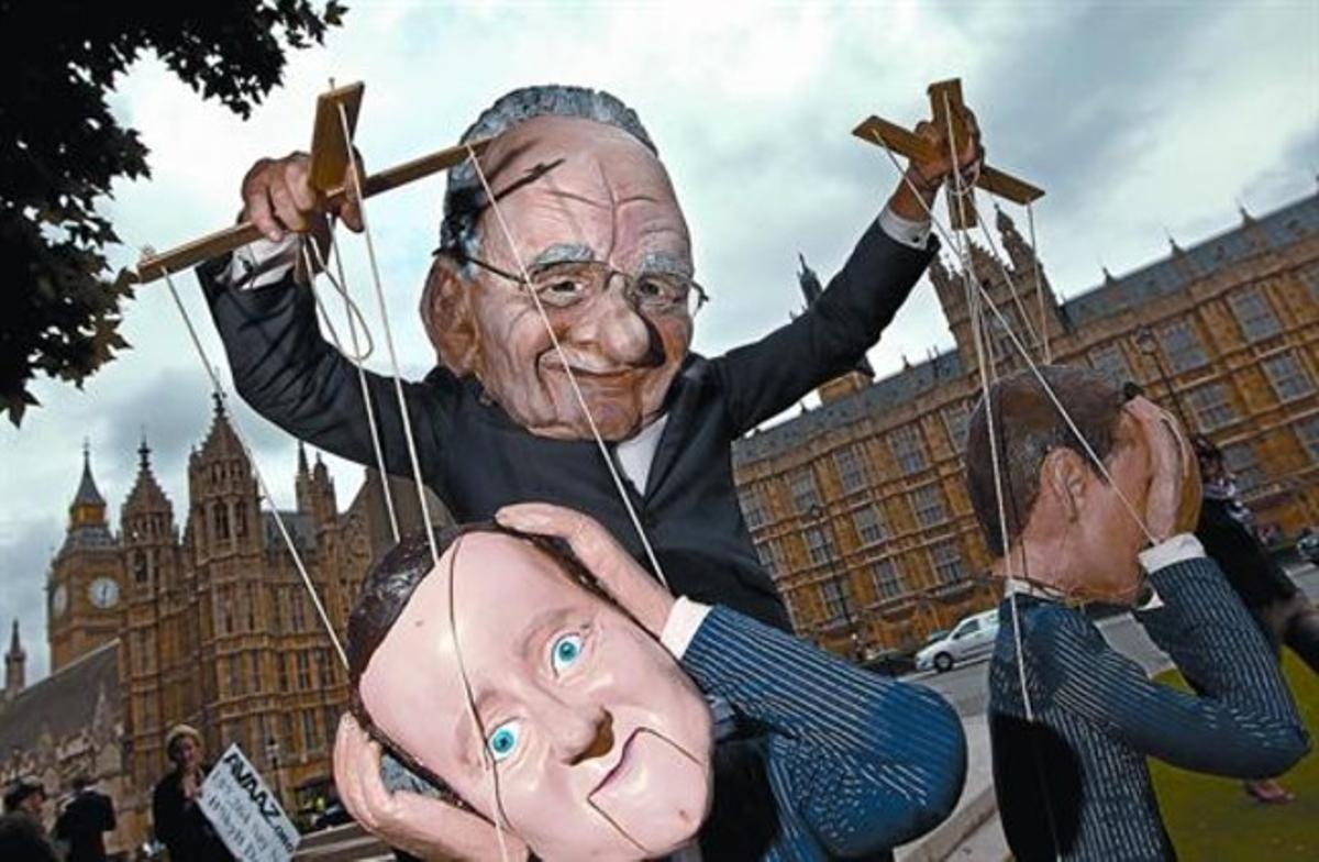 Un manifestante con una máscara de Murdoch, el dueño del imperio mediático del que aún forma parte ’News of the World’, mueve las marionetas del primer ministro Cameron y del titular de Cultura y Medios, Hunt, frente al Parlamento británico, el viernes.