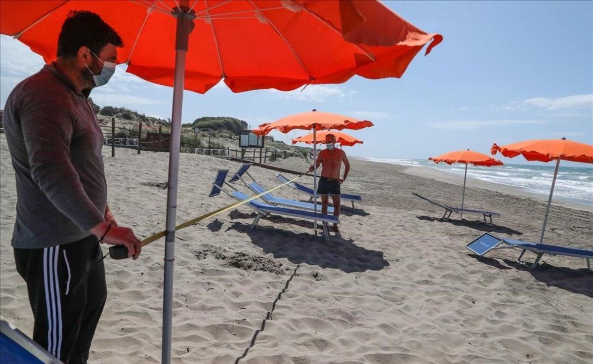 Dos trabajadores con mascarillas en la playa italiana de Copocotta, cerca de Roma. Dos trabajadores con mascarillas en la playa italiana de Copocotta, cerca de Roma.