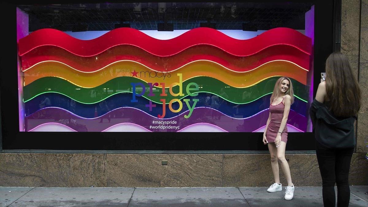 Una chica posa delante de un escaparate neoyorkino decorado con la bandera LGBTI en ocasión del día del Orgullo y el desfile del Pride