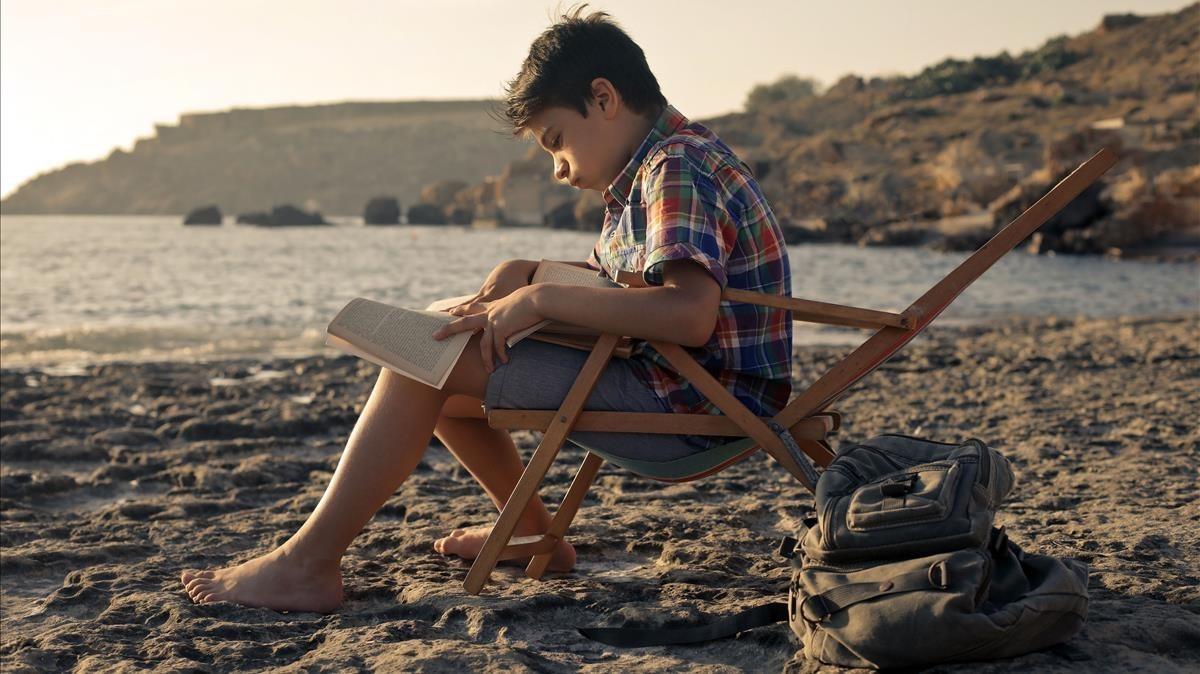 Un niño leyendo en la playa.