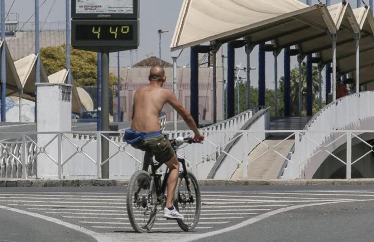 Un ciclista circula junto a un termóemtro a 44 grados en Sevilla.