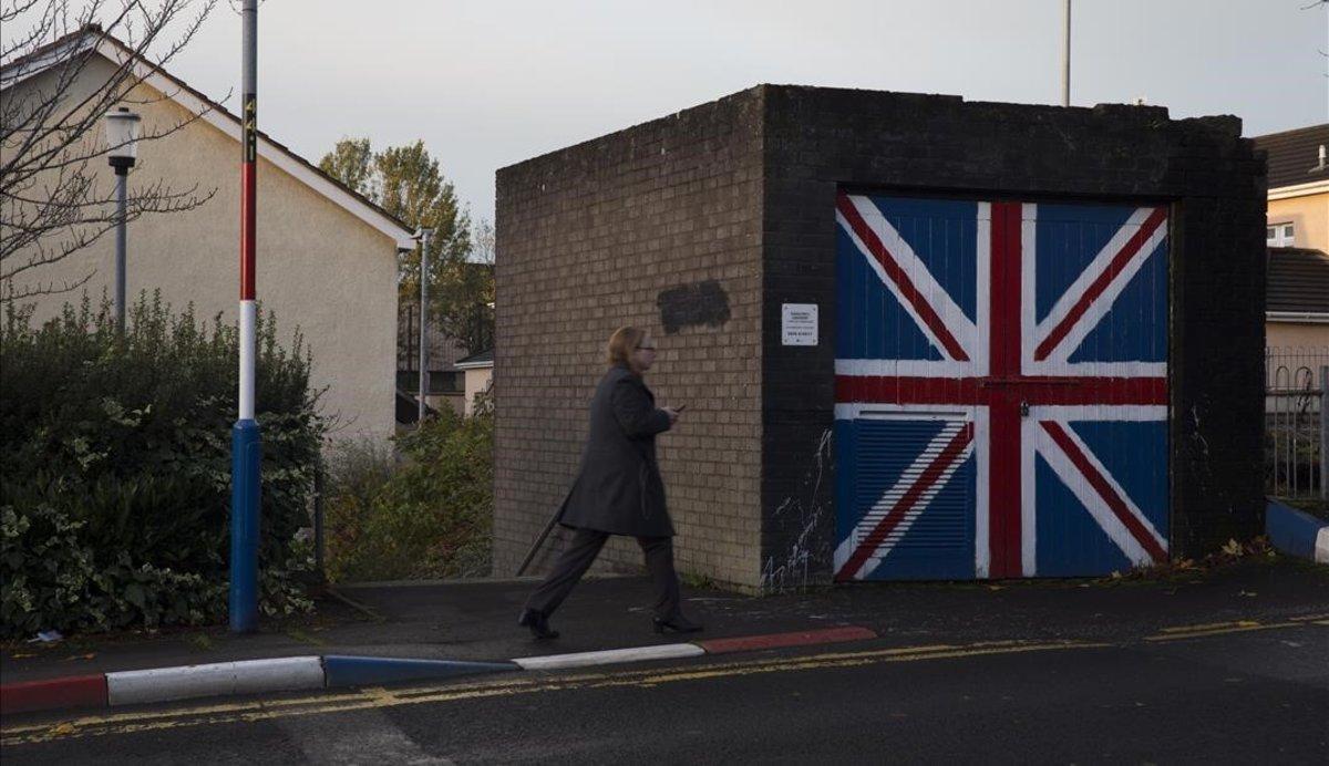 Una mujer pasa junto a un muro que luce la bandera de la Union Jack, en el barrio de Fountain West, en la localidad norirlandesa de Derry. 
