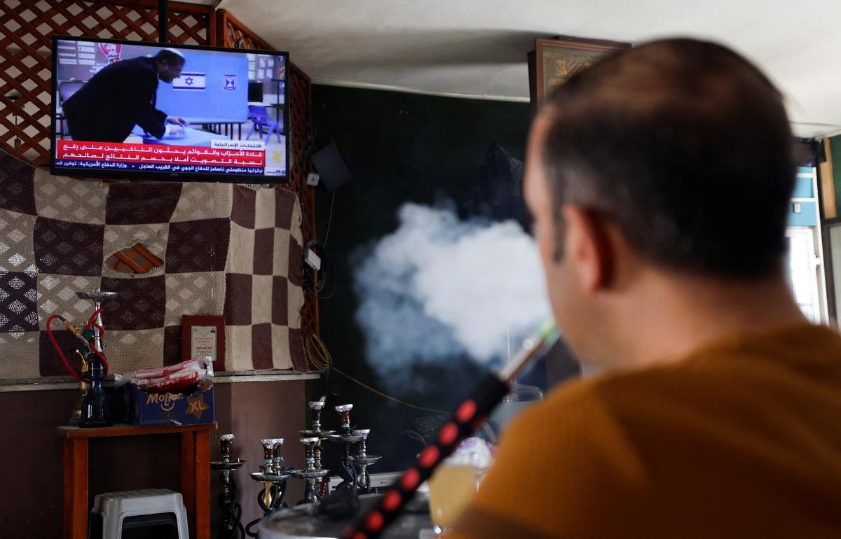 Un palestino fuma shisha mientras ve las noticias de televisión sobre las elecciones israelíes, en Hebrón, Cisjordania ocupada por Israel.
