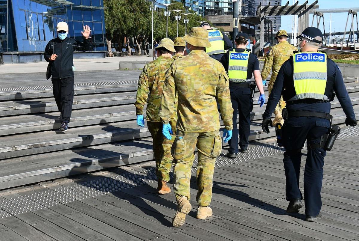 Un hombre saluda a un grupo de soldados y policías tras decretarse el toque de queda nocturno en Melbourne por covid-19.