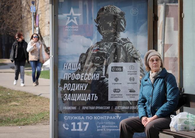 Una mujer espera el autobús junto a un póster que promociona el Ejército ruso, en Moscú.