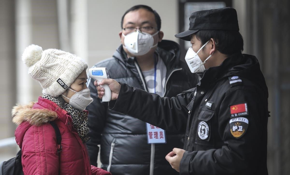 Personal de seguridad comprueba la temperatura coproral de los pasajeros en el muelle del río Yangtze, en la ciudad china de Wuhan. 