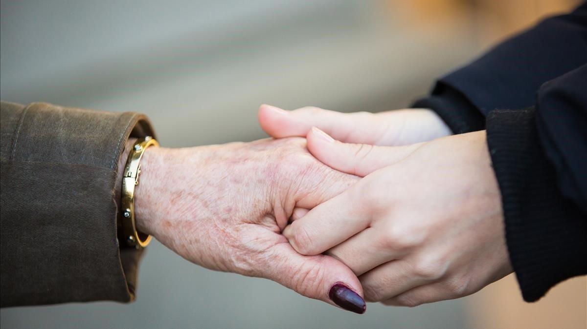 Una persona sostiene la mano de una mujer mayor.