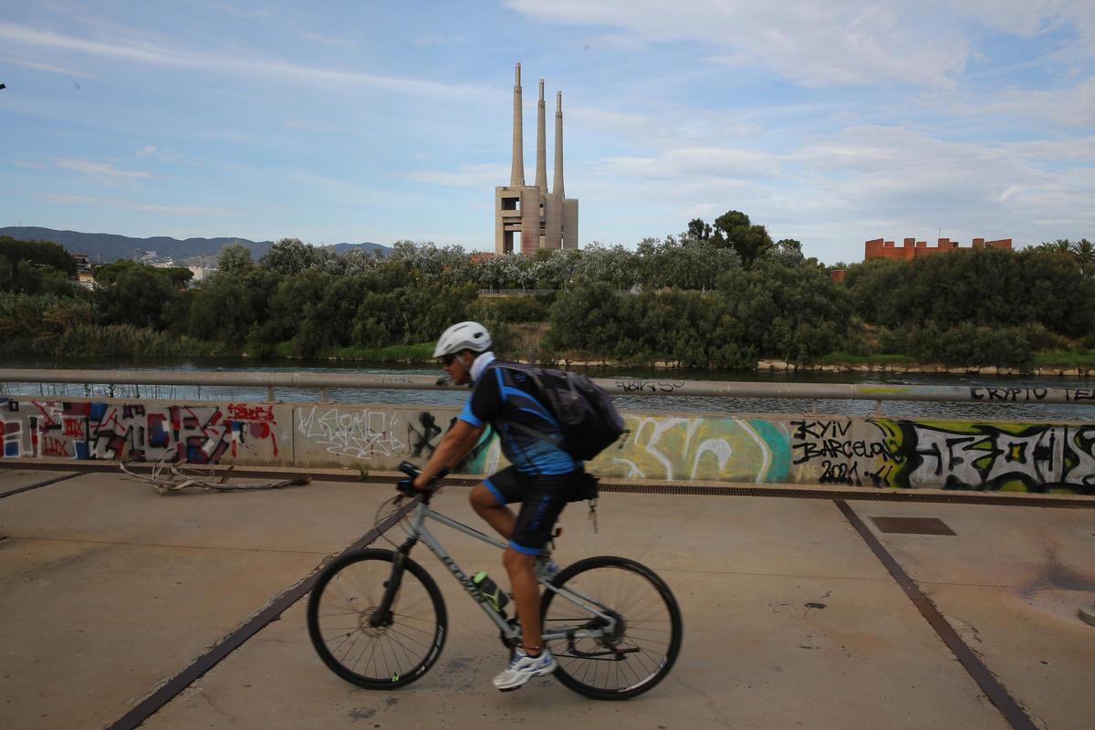 Un ciclista circula junto al río Besòs, con la antigua central térmica de las Tres Xemeneies al fondo. Un ciclista circula junto al río Besòs, con la antigua central térmica de las Tres Xemeneies al fondo.