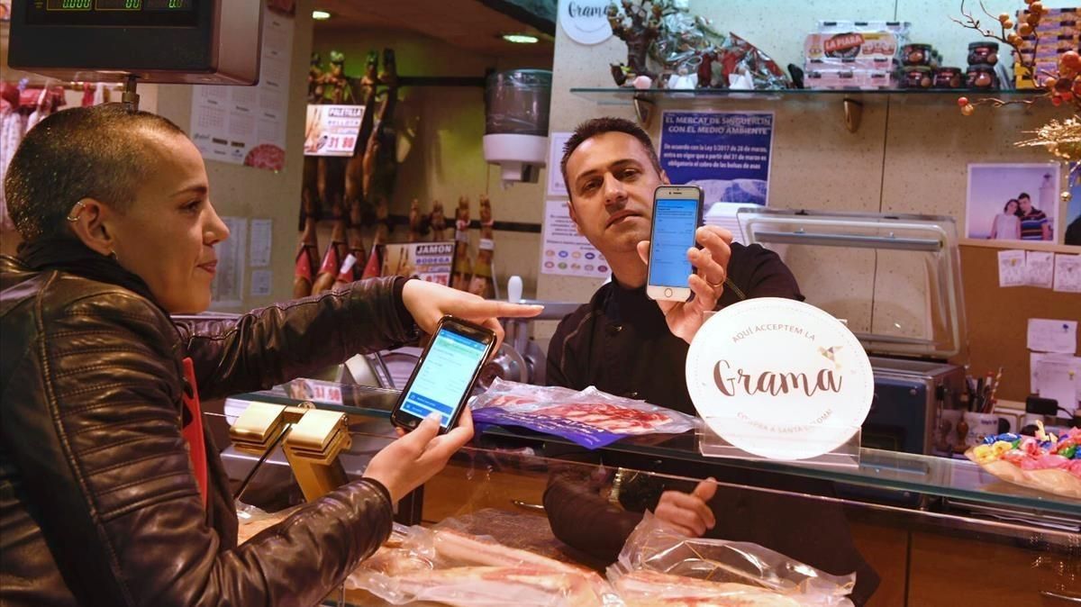 La presidenta de la Agrupació de Comerç de Santa Coloma, Laia Muñoz, simula un pago en la charcutería de Diego Navarro, en el mercado del Singuerlín, este miércoles. La presidenta de la Agrupació de Comerç de Santa Coloma, Laia Muñoz, simula un pago en la charcutería de Diego Navarro, en el mercado del Singuerlín, este miércoles.