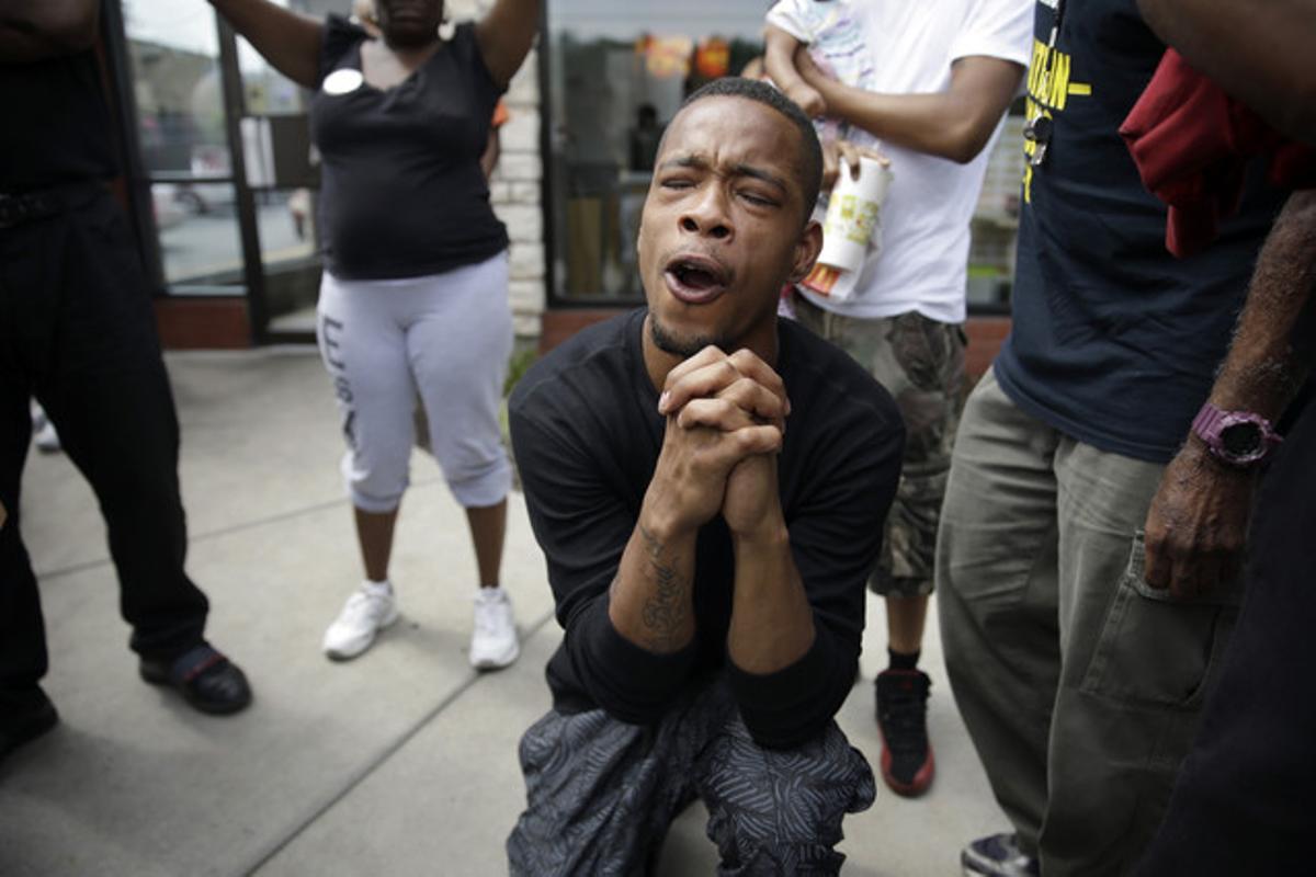 Un hombre reza mientras la policía dispersa a los manifestantes en Ferguson tras el asesinato de Michael Brown. Un hombre reza mientras la policía dispersa a los manifestantes en Ferguson tras el asesinato de Michael Brown.