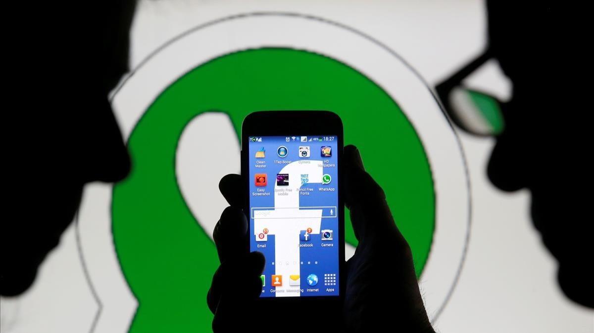 Dos hombres observan un ’smartphone’ con el logo de Facebook delante de una imagen del logo de Whatsapp.