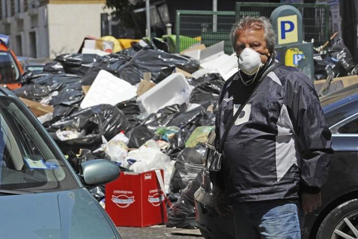 Un vigilante de un párking se protege del mal olor con una mascarilla, junto a un montón de basura sin recoger, en Nápoles. Un vigilante de un párking se protege del mal olor con una mascarilla, junto a un montón de basura sin recoger, en Nápoles.