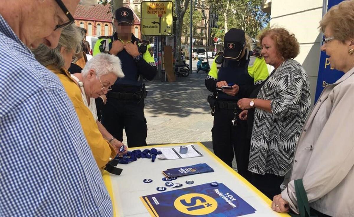 Dos guardias urbanos identifican a los miembros de una parada informativa sobre el referéndum, este sábado en Barcelona.