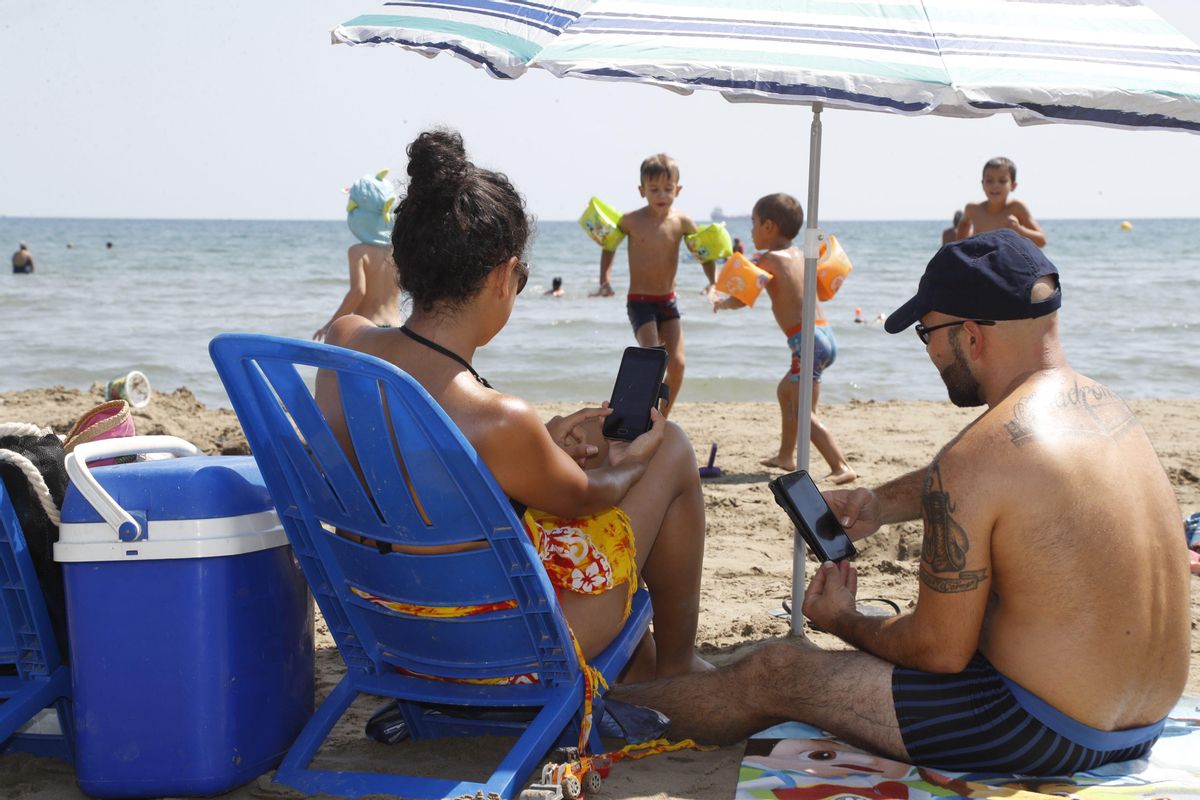 Dos personas consultan su teléfono móvil en la playa. Dos personas consultan su teléfono móvil en la playa.