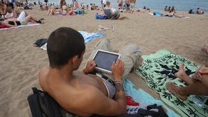 Un hombre consulta su tableta en la playa de Barcelona.